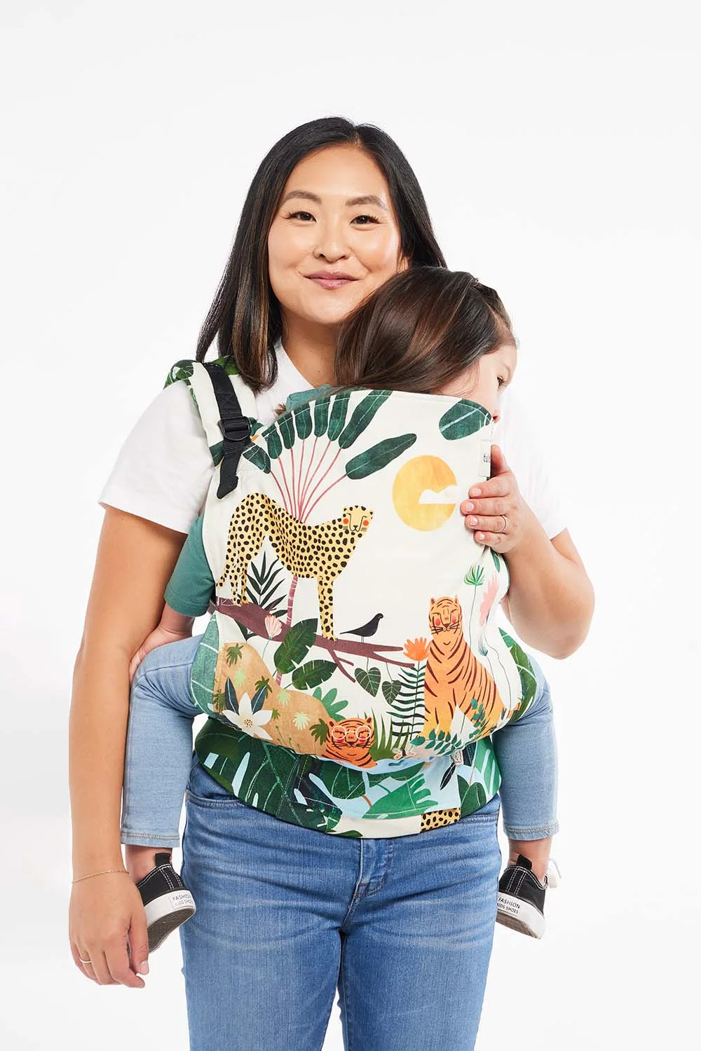Tula Baby Carrier Review: My Honest Experience and Favorites 6 Mother carrying her toddler in a colorful Tula Toddler Carrier featuring a jungle print with cheetahs, tigers, and tropical leaves. The structured panel and padded straps keep both parent and child comfortable during extended babywearing.