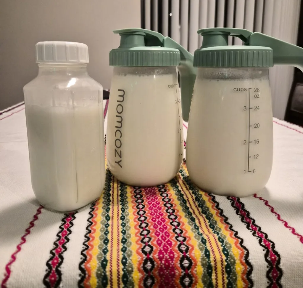 Three full bottles of pumped breast milk including two Momcozy wearable pump containers showing strong milk supply output