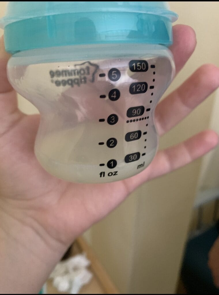 low-breastmilk-supply Hand holding a Tommee Tippee baby bottle with only 1 to 2 ounces of pumped breast milk