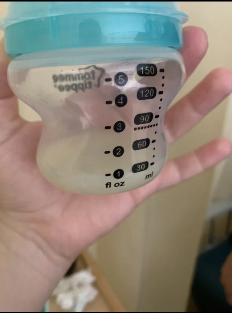 Hand holding a Tommee Tippee baby bottle with only 1 to 2 ounces of pumped breast milk